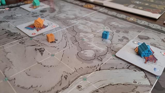 The main town board with lots of empty lots and a few building tiles. Wooden houses in player colours indicate who owns the buildings. There are little coloured markers on some lots indicating they were purchased by players.