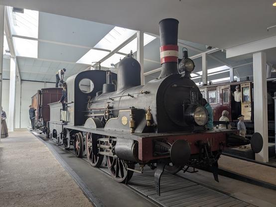 A photo of an old coal train inside a museum with lifesize human dolls with time accurate clothes on the train at the back