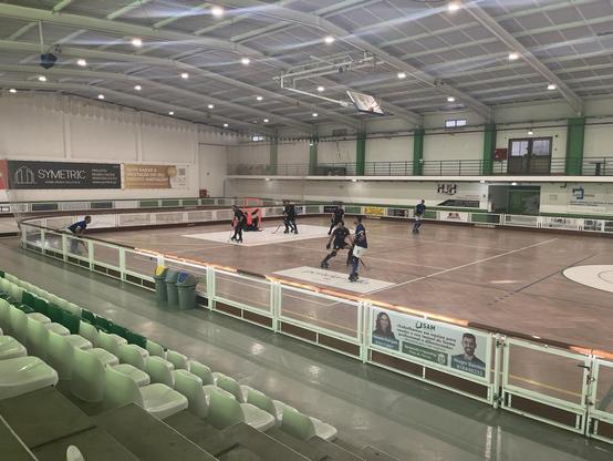 Foto de campo de hóquei em patins, onde se encontram duas equipas em jogo, uma vestindo azul e outra vestindo negro