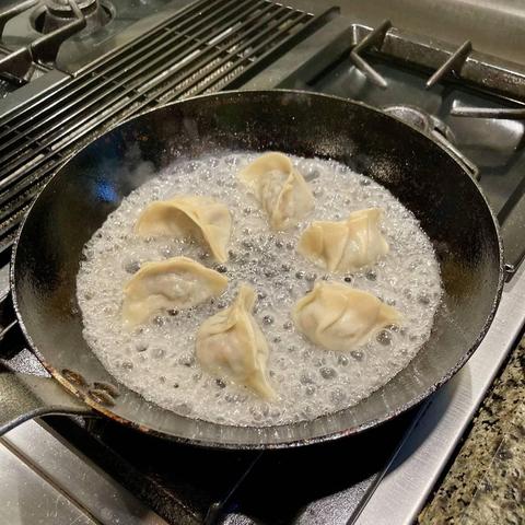 A photo of a pan on a stove. Six dumplings sit in a bubbling mixture of starch and water.