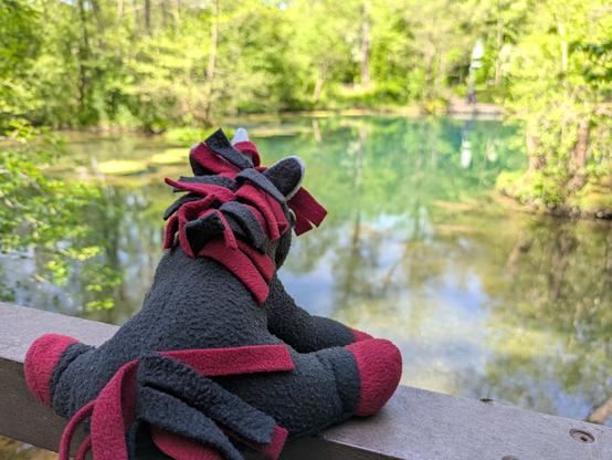 Einhorn im Vordergrund dahinter ein blauer Teich mit grünen Bäumen