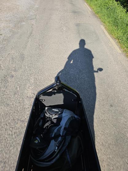 Picture of the cargo bay of a larryvsharry Bullitt bike long john cargo taken cycling eastwards with the sun behind the riser casting a Shadow of said rider