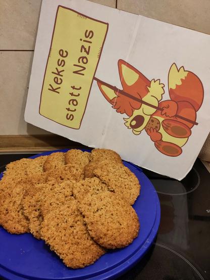 Auf einem Herd steht eine Platte mit selbst gebackenen Hafercookies. Dahinter lehnt ein Demoschild. Auf dem Schild ist ein Comic von @Fuchskind zu sehen. Es ist ein süßer sitzender Fuchs der an einem Keks knabbert. Er hält ein Schild auf dem steht: "Kekse statt Nazis".