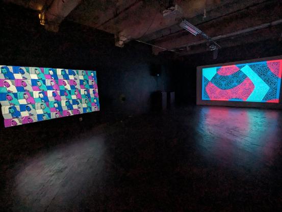A large dark room with two distant projections showing colorful patterns