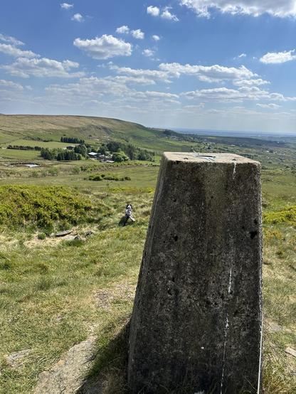 Moorland scene, a concrete trig point marker on top of a hill, looking down across a wide valley, a cocker spaniel walking down the hill
