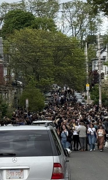 Urban street looking uphill.  Triple decker houses on both sides.  A crowd of people enjoying free live music played from various porches.
