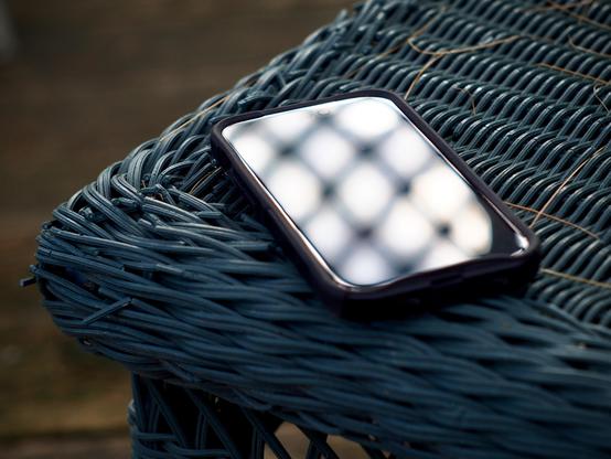 The glass face of a mobile phone reflects evening sunlight patterns as it rests on the corner of a blue wicker table