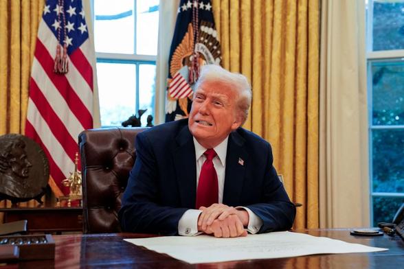 Former President Donald Trump sitting at his desk in the Oval Office, with a tense expression, during a signing event.
