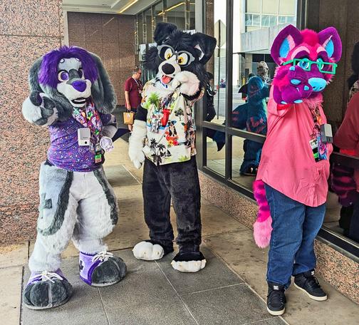 Three fursuiters are facing the viewer and pointing