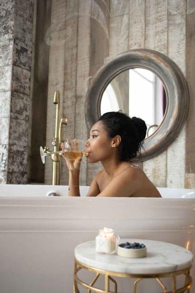 ethnic woman drinking white wine in bathtub