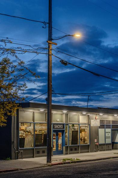 A photograph showing the striking color difference between the rising sun, a lone streetlamp, and the mildly-illuminated storefront of Sacks.