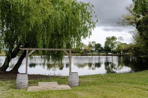A moody photograph of a simple wooden arch and stage in front of a lake and weeping willow.