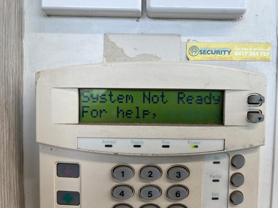 Photo of an older home alarm system panel with the display: 
System Not Ready
For help,