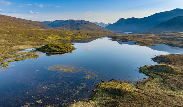 A still blue loch surrounded by hills and mountains.