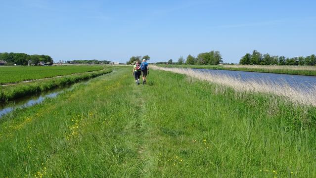 Twee wandelaars op een grasdijk langs een kanaal.