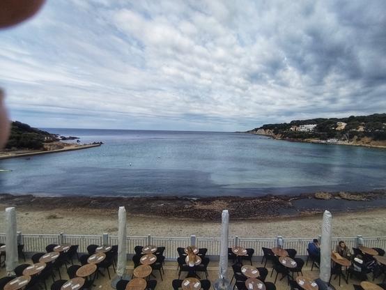 Plage de Portissol (ou Port Issol) sous un ciel couvert. Mer calme. À droite la Kima et la pointe de la Cride. Premier plan, une terrasse de bar se met en place.