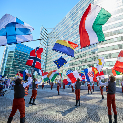 Photo of people in traditional costumes throwing large flags of different European Union Member States in the air.