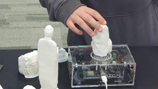 A child places a 3D printed object onto a transparent Museum in a Box.