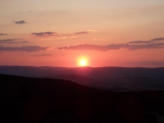 Saying goodnight to the sun as it sets behind a distance hill. The sky is a nice orange colour.