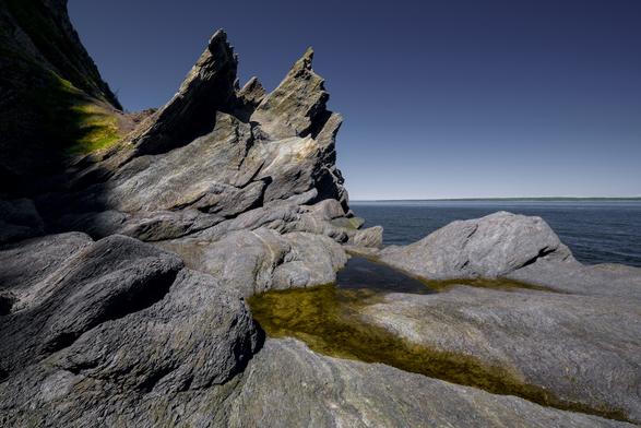 Jagged rocks point upwards at the foot of a cliff overlooking the Saint-Lawrence river in Le Bic provincial park in Quebec, with a small shallow pool of water at their base.