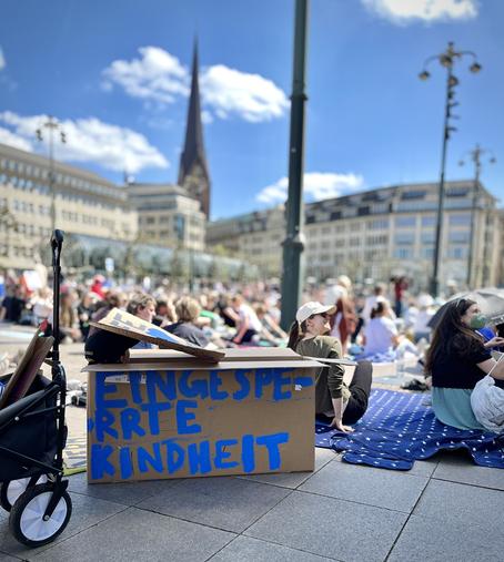 Kind sitzt in einem Pappkarton mit der Aufschrift „eingesperrte Kindheit“
