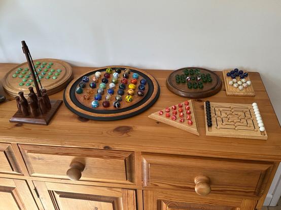 A wooden chest with a flat surface, holds seven games, all wooden, with different coloured marbles.