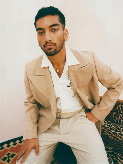 Nabhaan Rizwan, actor moreno de piel y pelo, con barba y bigote, lleva un traje color crema, posa sereno y estiloso.