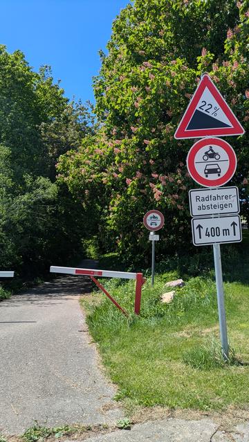Foto einer beschrankten Straße mit Radfahrer-absteigen-Schild kombiniert mit 22% Gefälle-Schild