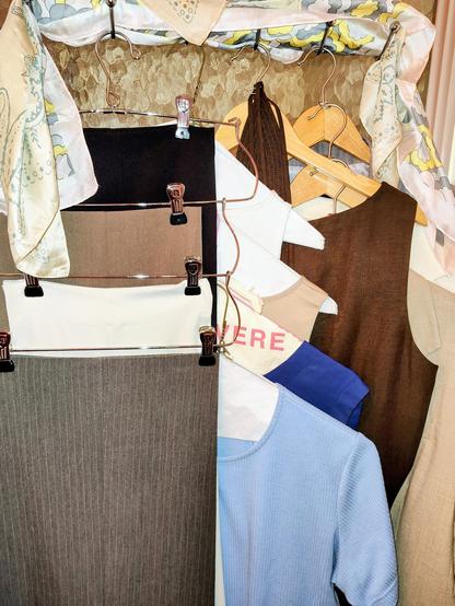 A bunch of work clothes hanging up. Tops: pale blue T, navy blue shell, beige shell, white knit boat neck shell. Trousers: grey pinstripes, white satin, taupe, black. Brown silk blend shell dress. Blazers: beige, white, grey. A couple silk neckerchiefs in beige, blue, grey, and yellow.