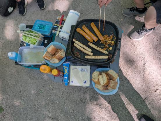 Auf einem sandigen Platz werden Würsrchen und Zwiebeln gegrillt