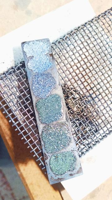 Des teintes d'émail sur une petite plaque d'acier posée sur une grille.
Du gris clair au céladon foncé en passant par un vert sapin.
