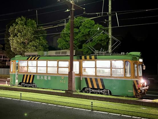 A green and yellow tram with 散水電車 written on it and a bunch of pipes and metalwork inside it