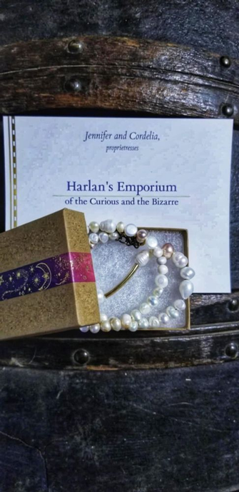 Image description by TCBR: A beautiful pearl necklace in the fashion of Ed's from Season 2 of Our Flag Means Death. It is in its protective box, set on a wooden trunk with a tag from Harlan's Emporium of the Curious and Bizarre.