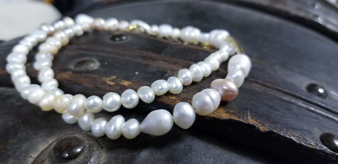 Image description by TCBR: A beautiful pearl necklace in the fashion of Ed's from Season 2 of Our Flag Means Death. It is set on a wooden trunk.