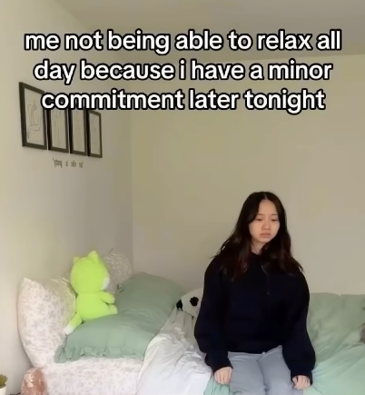 A woman sitting on her bed, looking vaguely sad and concerned, with a caption of "me not being able to relax all day because i have a minor commitment later tonight"