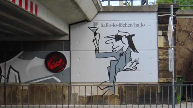 Teil der Udo-Lindenberg-Collage an der Unterführung in Radebeul/West 

Udo Lindenberg (Comic) in grau/weiß/schwarz sitzt und hält in seiner rechten Hand ein Glas Eierlikör.
In der li ken Hand, die aufgestützt wirkt, die Zigarre.

'Hallo-lo-löchen hallo' steht drüber.