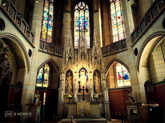 Altaransicht der Schlosskirche in Wittenberg mit reich verziertem Hochaltar im neugotischen Stil, umgeben von farbenprächtigen Glasfenstern und steinernen Heiligenfiguren.