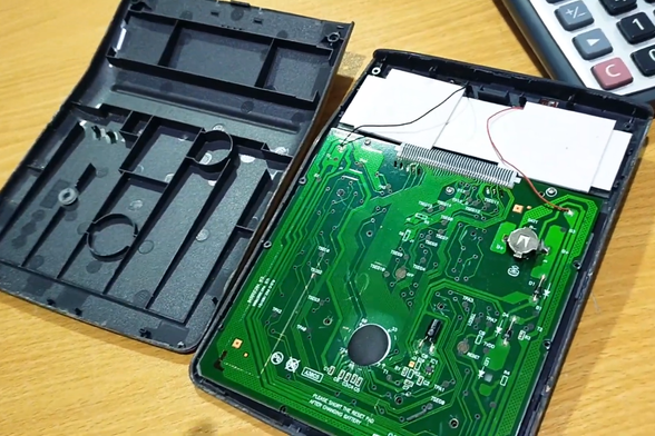 Calculadora Casio DX-12B abierta y mostrando el reverso de la plaqueta de circuito integrado con el portapila de hojalata ajustable y una pila A76.