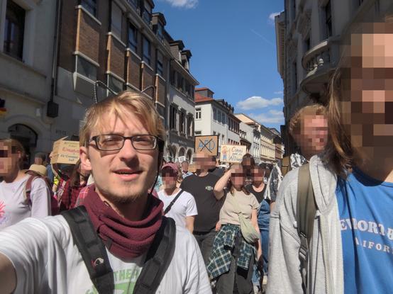 A selfie of me, a white guy with bleached hair, black 3d-printed cat-ears and black rectangular glasses, walking in a crowd of protestors. All faces except mine are pixelated. The visible signs say:
- "AfD" crossed out
- "Conni geht die AfD ärgern"
- "Menschenrechte statt rechte Menschen"
- "Miliardärs-<unlesbar>, Klimaschutz, EU-Zusammenhalt"
- "Björn Höcke ist ein Nazi"