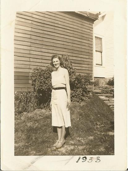 A tall young lady in a white dress standing in front of a barn.