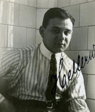 A photo of a young man in a striped shirt and a tie. He has long hair. He is photographed against the background of bright tiles.