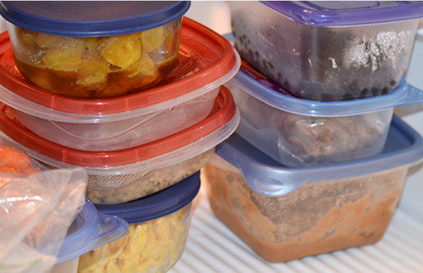 Color image of color-lidded clear containers full of leftover food, on a refrigerator shelf.
