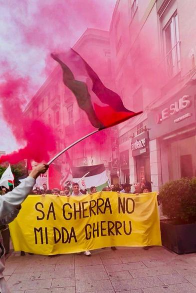 Foto della manifestazione di Cagliari. Striscione: "Sa gherra no mi dda gherru". Bandiere della Palestina in primo piano.