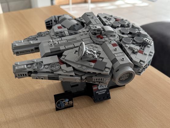A detailed LEGO model of the Millennium Falcon is displayed on a stand with a Star Wars logo.