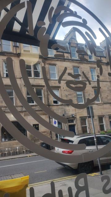 Looking through the window of Jan's Bubbles, with the outline of a smiling face drawn on the glass, a Victorian stone tenement visible opposite