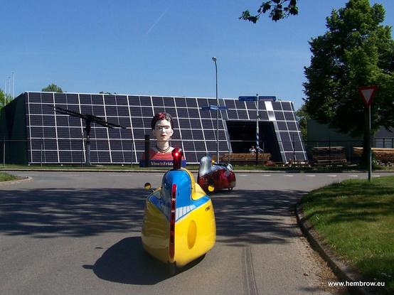 A bust of Frida Kahlo, five metres or so in height, in front of a building covered in solar panels.
