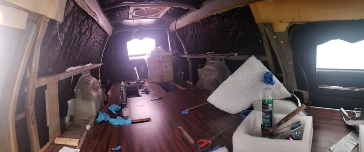The inside of a hearse lined with black thinsulate between its metal ribs. Various construction materials are laying around the vehicle's floor.