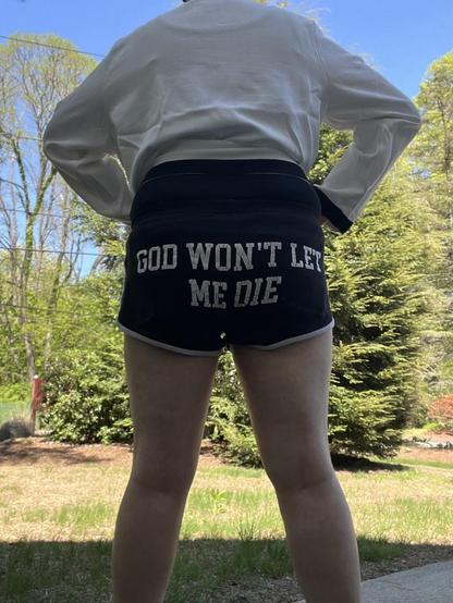 me in the same outfit, turned around. viewers can now see that the booty shorts say GOD WON’T LET ME DIE across the butt.