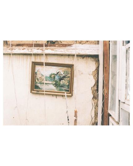 in the center an old picture frame inclined on a white shabby wall. right hand side white window frames. from the ceiling are white ropes hanging