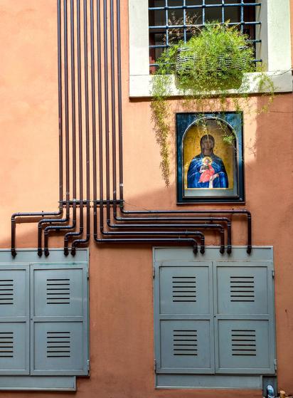 A painting of the Christ and Holly Maria on an orange street wall where lots of metal pipes are set and seem to turn around the painting